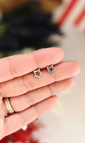 Hand holding two star-shaped earrings with a blurred background